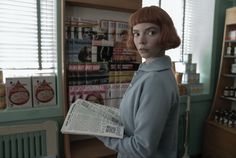 a woman standing in front of a store holding a newspaper and looking at the camera