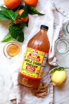 a bottle of apple cider vinegar sitting on top of a towel next to some oranges