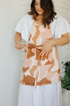 a woman is wearing an apron and holding a pair of scissors in one hand while standing next to a potted plant