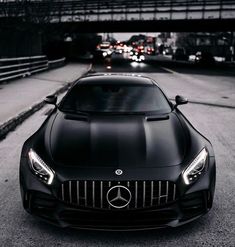 a black mercedes sports car parked in front of a bridge with traffic on the other side