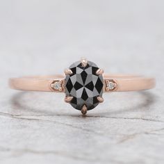 a black and white diamond ring sitting on top of a stone slab with two diamonds around it