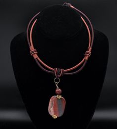 "A multi-strand fabric cord necklace with a rectangular pendant of red jasper beneath a faceted red jasper bead. The Necklace has a round white stone bead as a clasp that can be inserted for three different sizes.  Pendant - 3 x 1 1/8\" Necklace - 15 1/2, 17 1/4, or 19 inches long" Artisan Adjustable Rectangular Necklace, Artisan Rectangular Adjustable Necklace, Red Rectangular Adjustable Jewelry, Red Jasper Necklaces, Handmade Jasper Round Pendant Jewelry, Unique Red Jasper Necklaces, Artisan Red Jasper Jewelry, Unique Jasper Pendant Jewelry, Red Jasper Pendant