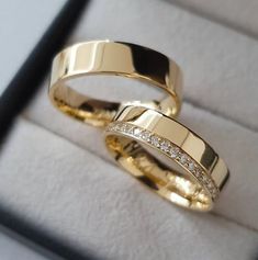 two gold wedding rings sitting on top of each other in a ring box with diamonds