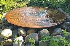 a bowl shaped fountain surrounded by rocks and plants