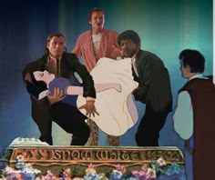 three men standing on top of a cake in front of another man holding a guitar