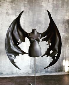 a mannequin's torso with black wings on a metal stand in front of a concrete wall