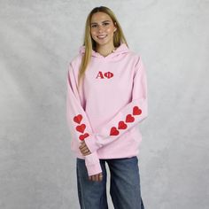 Alpha Phi hoodie in pink with super cute red hearts on the sleeve might just be the cutest design we carry this year. With the Alpha Phi Greek letters printed on the front and Alpha Phi since 1872 on the back it's a must-have addition to your wardrobe. With it's classic, unisex fit and a practical pouch pocket this versatile sweatshirt can be styled with everything on or off campus, whether studying, relaxing or hanging out with your sisters. Crafted from premium materials for comfort and warmth this sorority sweatshirt is perfect for layering or wearing on it's own. Part of our new 2024/2025 collection. Alpha Phi Hoodie Sizing Model is 5'9", size 0/2, and wearing size M A Phi Hoodie Technical Details  - Jersey lined hoodie  - Pouch pocket  - Unisex sizing  -  Sustainable Manufacturing  - Casual Long Sleeve Sweatshirt For Valentine's Day, Valentine's Day Casual Long Sleeve Sweatshirt, Red Long Sleeve Sweatshirt For Valentine's Day, Pink Fitted Hoodie Top, Pink Fitted Sweatshirt For Spring, Fitted Pink Sweatshirt For Spring, Fitted Long Sleeve Pink Hoodie, Cute Pink Hoodie For Loungewear, Cute Pink Loungewear Hoodie