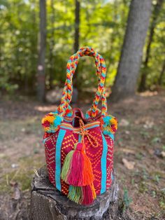 This beautiful and vibrant Wayuu shoulder bag is a large, handcrafted piece made by the skilled artisans of the Colombian Wayuu tribe. The bag features bold, colorful designs with intricate geometric patterns woven in rich red, orange, turquoise, and yellow hues. The braided straps incorporate the same vibrant colors, creating a cohesive and eye-catching look. Decorative pom-poms and tassels add playful texture and detail to the bag, making it a perfect statement accessory.  This unique bag is ideal for those looking for a pop of color and culture in their wardrobe, and it makes an excellent, one-of-a-kind gift. Perfect for daily use or as a standout piece for special occasions, it's a beautiful blend of traditional craftsmanship and modern style. Excellent quality, check-out the durabilit Wayuu Bags Pattern, Wayuu Bag, Braided Strap, Unique Bags, Bag Pattern, Purses And Handbags, Pom Pom, Vivid Colors, Color Design