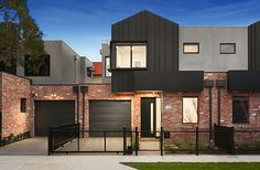 two story brick house with black iron fence and gated yard at dusk, surrounded by green grass