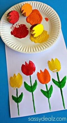 a paper plate with flowers and leaves on it next to a white paper plate that has red, yellow, and orange flowers