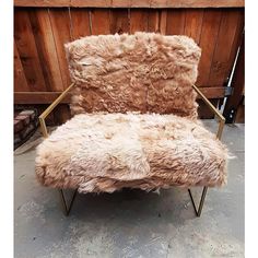 a chair that is made out of sheepskin and has metal legs, sitting in front of a wood paneled wall