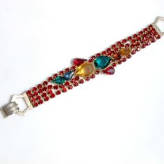 Fabulous Julianna or Julianna style bracelet that features four strands of prong set, deep red rhinestones and a front panel of multicolored, tear-drop shaped stones. The two largest stones have open backs, the rest have closed backs and are foiled. Gold tone metal, fastens securely with a fold-over clasp. Measures 7 1/4 inches long and just under 1 inch at the widest point in the front. The largest stone measures just over 5/8 of an inch by 1/2 of an inch. All the stones are present and in good Red Crystal Rhinestone Bracelet For Party, Red Jeweled Bracelet For Party, Red Rhinestone Crystal Bracelet For Party, Red Crystal Bracelet With Rhinestones For Party, Red Rhinestone Bracelets For Party, Red Crystal Bracelets With Rhinestones, Red Jubilee Bracelets For Parties, Red Jubilee Bracelet For Party, Adjustable Red Bracelet With Rhinestones