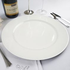 a white plate with silverware and a bottle of wine next to it on a table