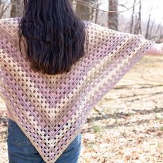 a woman wearing a pink crocheted shawl in the woods with her back to the camera