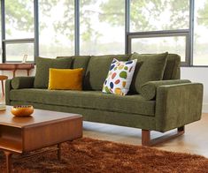 a green couch sitting in front of a window next to a wooden table and chair