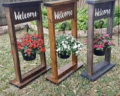 three wooden planters with flowers in them on the grass and one has a welcome sign