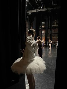 a woman in a white tutu is looking at her cell phone while dancers are on the other side