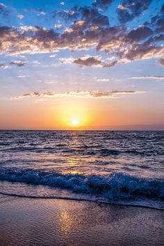 the sun is setting over the ocean with waves coming in to shore and blue sky