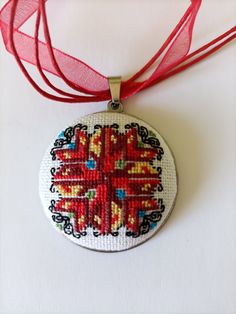 a cross stitched ornament hanging from a red ribbon on a white surface