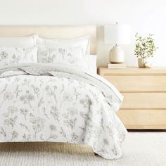 a bed with white and grey floral comforter set on top of it in a bedroom