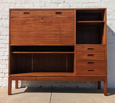 a large wooden cabinet sitting on top of a sidewalk next to a white brick wall