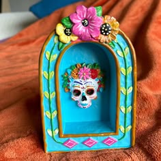 a colorful skull in a blue frame with flowers on it's head sitting on an orange blanket