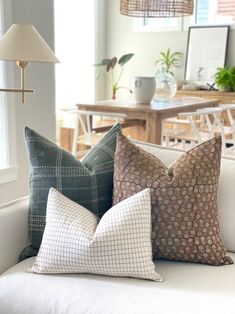 four pillows are sitting on a couch in front of a table with chairs and a lamp