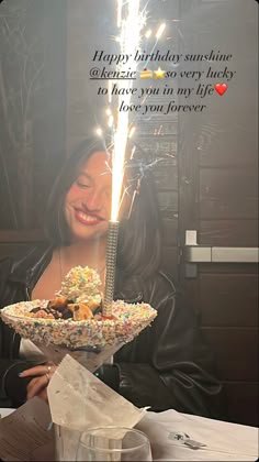 a woman sitting at a table with a cake in front of her and sparklers above her head