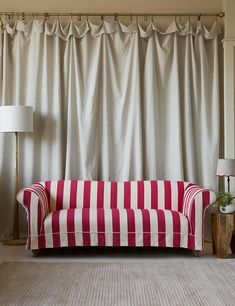 a red and white striped couch sitting in front of a window with curtains behind it