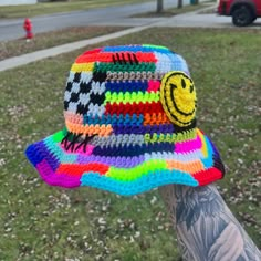 a multicolored hat with a smiley face drawn on it is held up by someone's arm