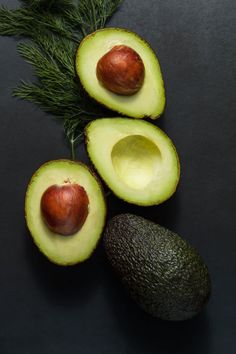 an avocado cut in half next to two pieces of fruit on a black surface