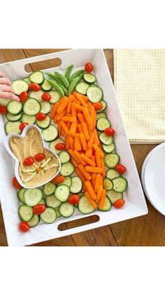 a tray filled with cucumbers, carrots and hummus on top of a wooden table