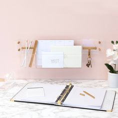 a binder, notepad and pen on a marble desk with pink wall in the background