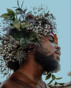 a man with flowers on his head looking up at the sky in front of him