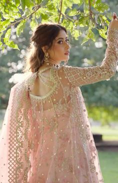 a woman in a pink dress standing under a tree with her hands on the branches