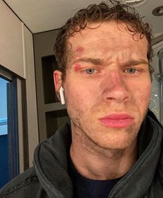 a man with ear buds on his ears looking at the camera while he is in front of a mirror