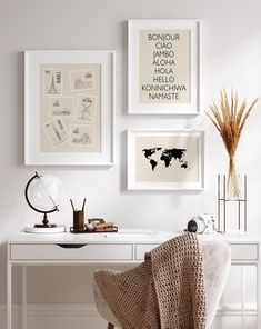 three framed pictures hang on the wall above a white desk with a chair and lamp