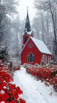 a red church with a steeple surrounded by trees and flowers in the snow covered ground