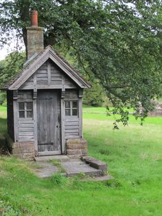 an old outhouse sits in the middle of a grassy field with a brick chimney