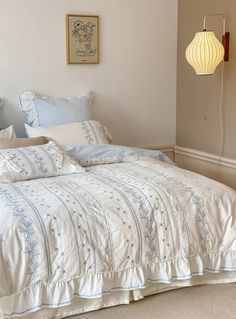 the bed is made with white linens and blue embroidered sheets, along with two lamps on either side