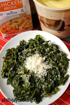 a white plate topped with spinach and cheese next to a container of chicken broth