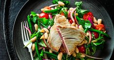 a plate with meat, beans and veggies on it next to a fork