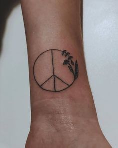 a peace sign tattoo on the wrist with flowers and leaves around it, in front of a white background