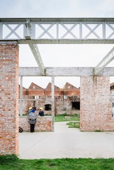 a person standing under an overpass in the middle of a field with brick buildings behind them