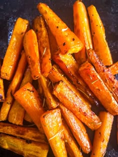 some cooked carrots on a black plate with seasoning sprinkled around them