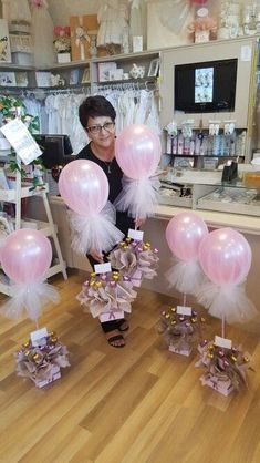 a woman standing in front of pink and white balloons with bows on them, at a store