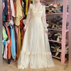 a woman is standing in front of a rack of shoes and dresses on racks, wearing a long white dress with ruffles