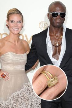 a man and woman standing next to each other in front of a white wall with an engagement ring on it