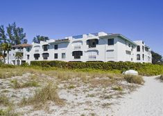 an apartment building on the beach with grass and bushes