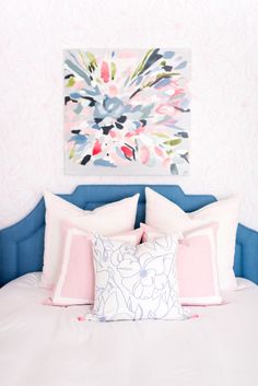 a bed with pink and blue pillows in front of a colorful painting on the wall